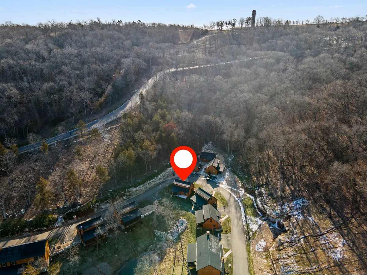 This image showcases multiple wooden cabins nestled among rolling hills and trees, connected by a winding road. The peaceful scene suggests opportunities for hiking, nature walks, and photography, especially as the foliage is beginning to turn color.