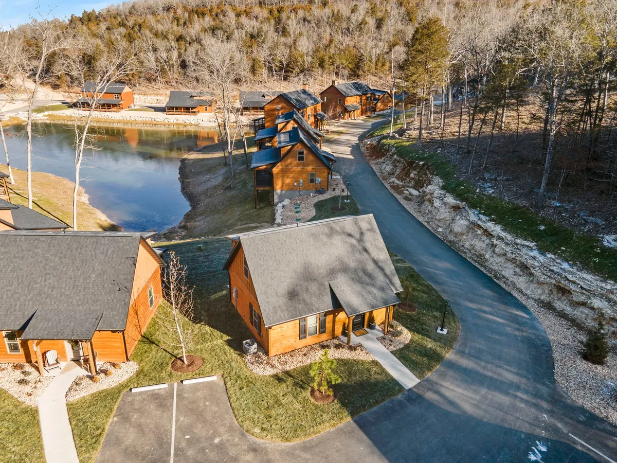 A lakeside view with cabins nestled along the shore and a tree line reflected in the calm water. The serene lake offers opportunities for fishing, boating, and peaceful mornings, while the cabins establish a sense of rustic comfort and community within the natural setting.