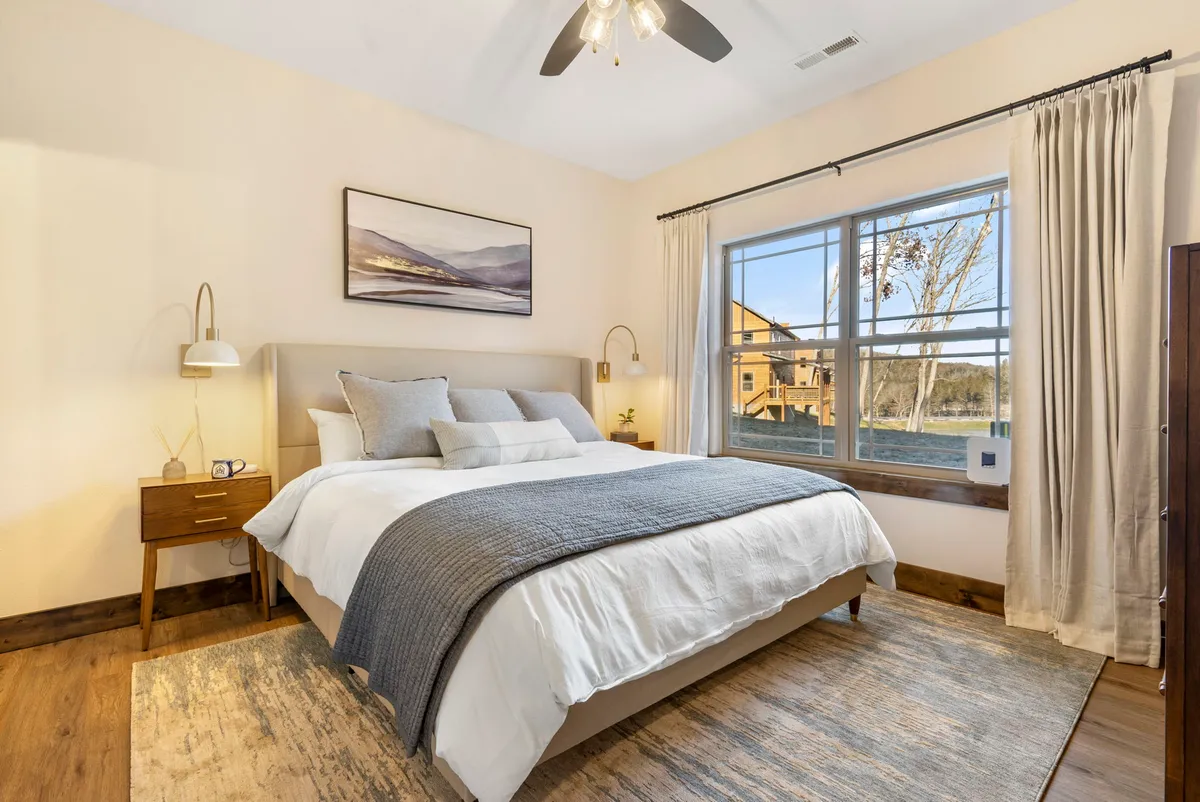 A serene bedroom with a king-sized bed adorned with decorative pillows, a window allowing daylight to filter in, and tasteful wall art adding a touch of elegance.