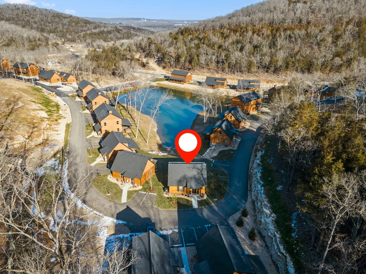 An aerial perspective shows the central house with a marked location, surrounded by additional cabins, a pond, and ample green space. The composition emphasizes the close integration of the cottages with the natural landscape, highlighting open areas for family gatherings and outdoor activities.