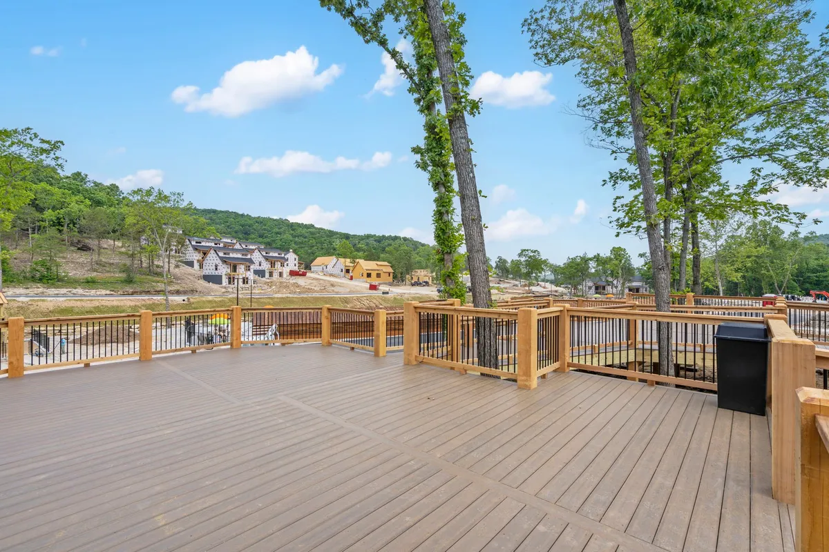 A peaceful wooden deck nestled among mature trees, with a view of distant houses almost hidden by the lush greenery. The deck is perfect for relaxing outdoors and offers a secluded vantage point to appreciate the natural surroundings.