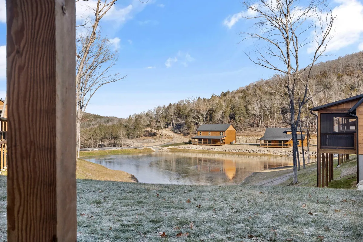 A tranquil lakeside view with cabins nestled among trees, a serene lake reflecting the sunset, and mountains in the distance. Activities like fishing, boating, and hiking are subtly suggested by the setting.