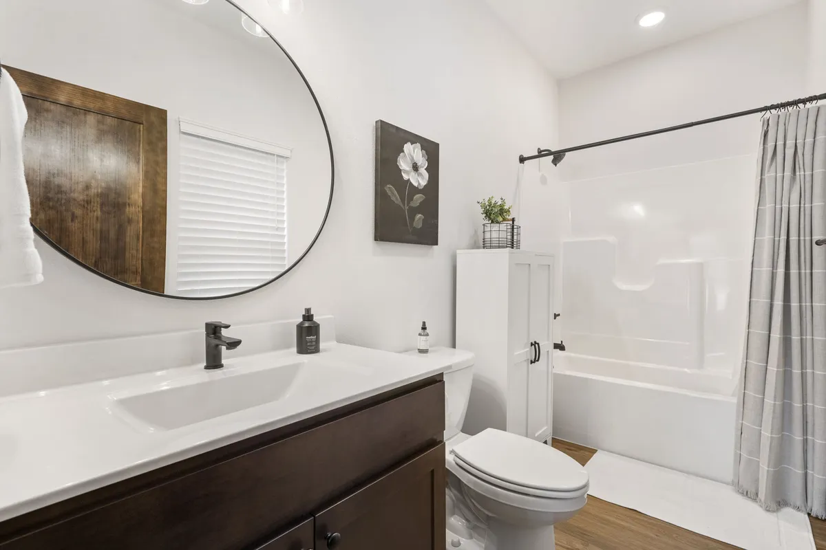 A modern, sparkling bathroom with a round mirror, stylish vanity, artwork, and a glass shower, exuding a calm and inviting mood.